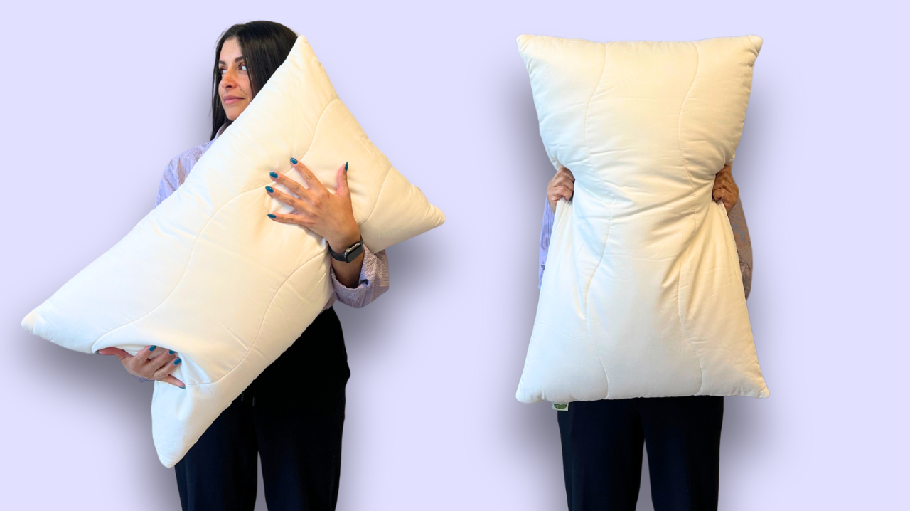 Two people holding large pillows against a light purple background