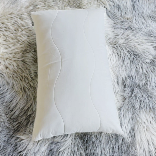 A white latex pillow placed on a grey furry surface.