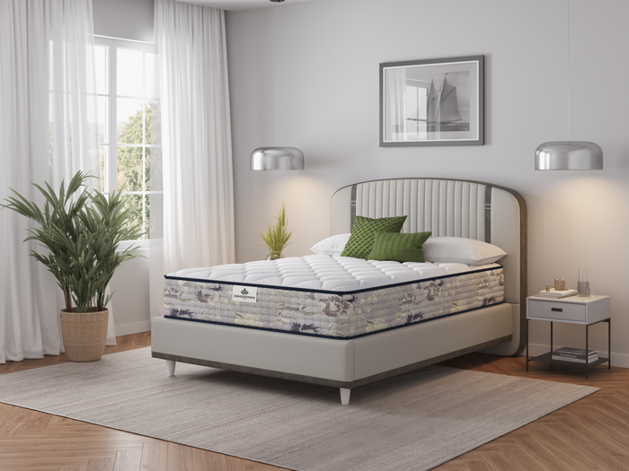A Kingsdown Rome Tight Top Firm mattress in a bedroom setting, showcasing the mattress with pillows on it, placed between two nightstands with lamps, in front of a window with curtains.