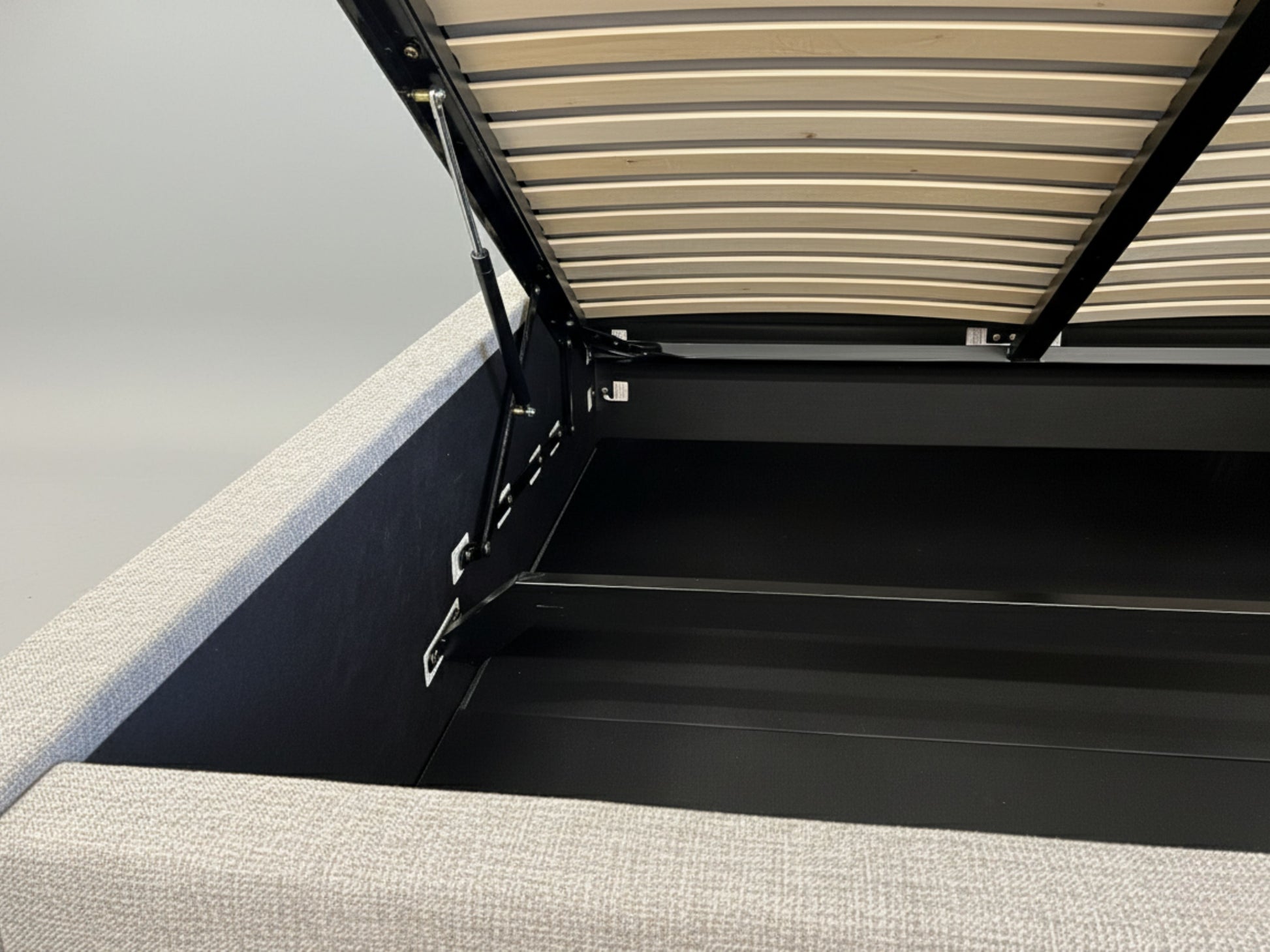 Gray upholstered bed with a black metal frame and wooden slats.